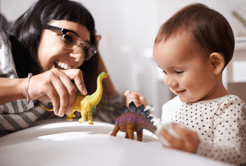 Parent and child engaged in play with toy dinosaurs, illustrating interactive early intervention techniques.